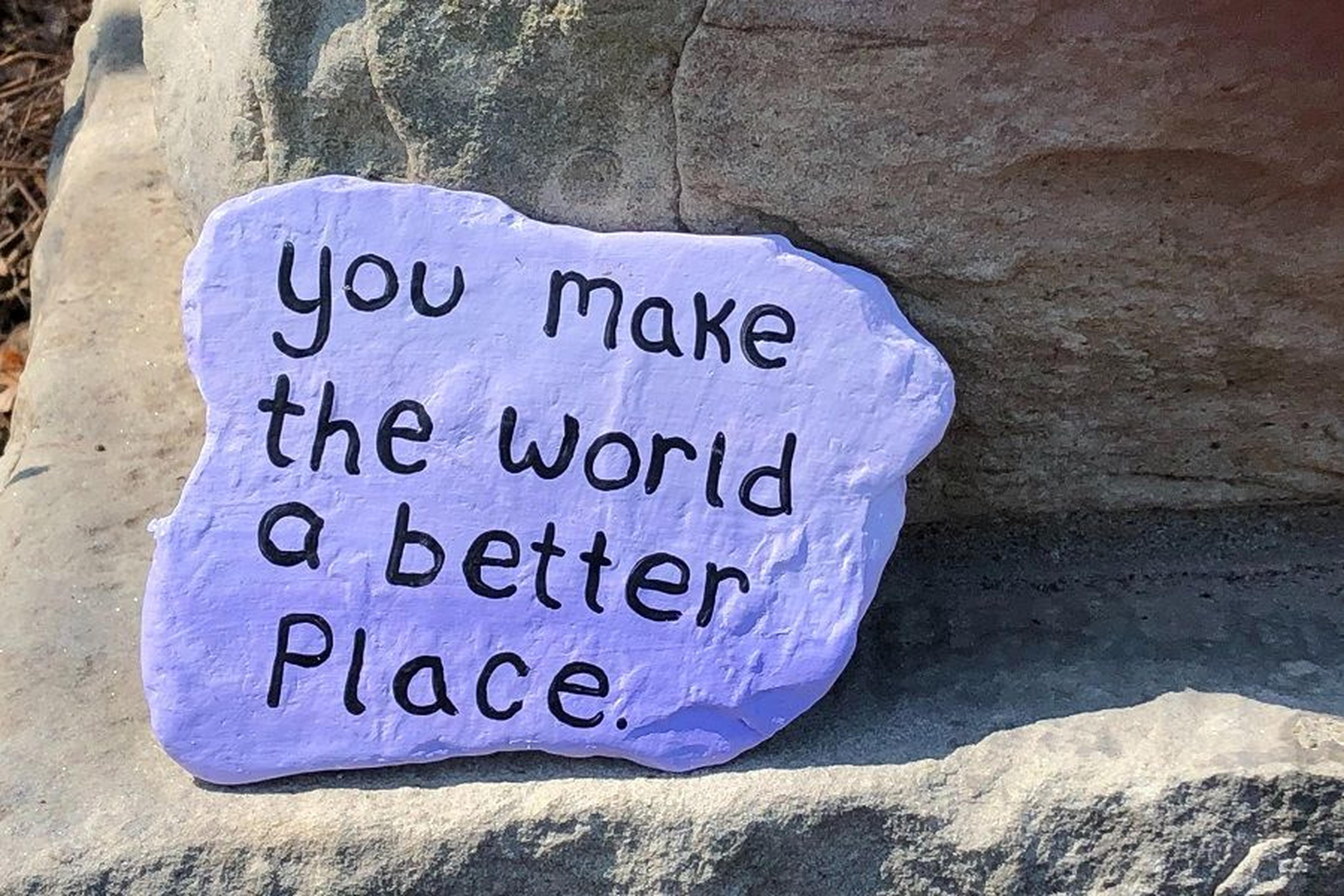 Handbemalter Stein mit der Aufschrift „you make the world a better place“ liegt auf einem Felsen.