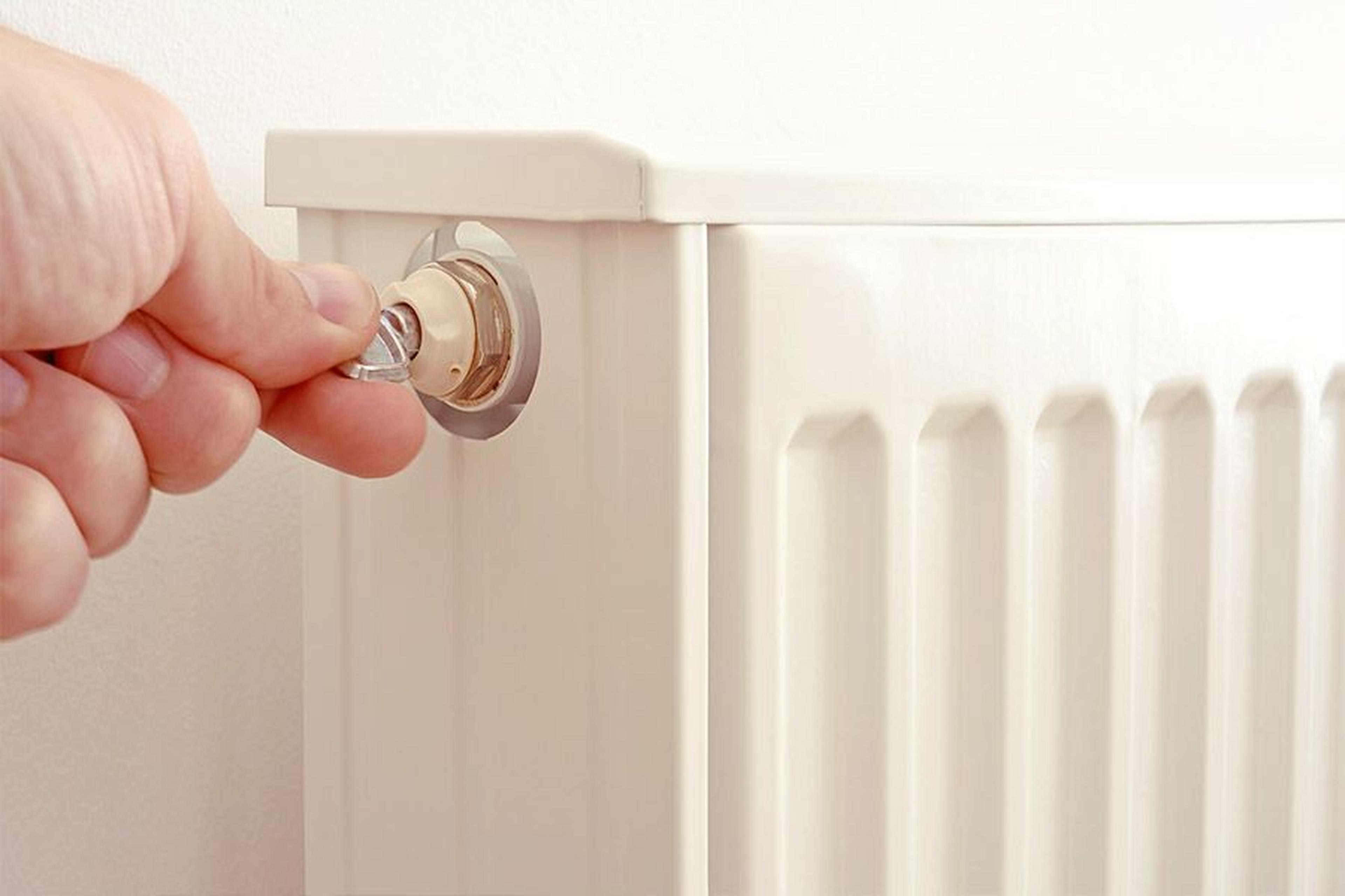 Eine Hand, die mit einem Schlüssel einen weißen Heizkörper entlüftet und dabei die eingeschlossene Luft aus dem Ventil an der Seite ablässt.