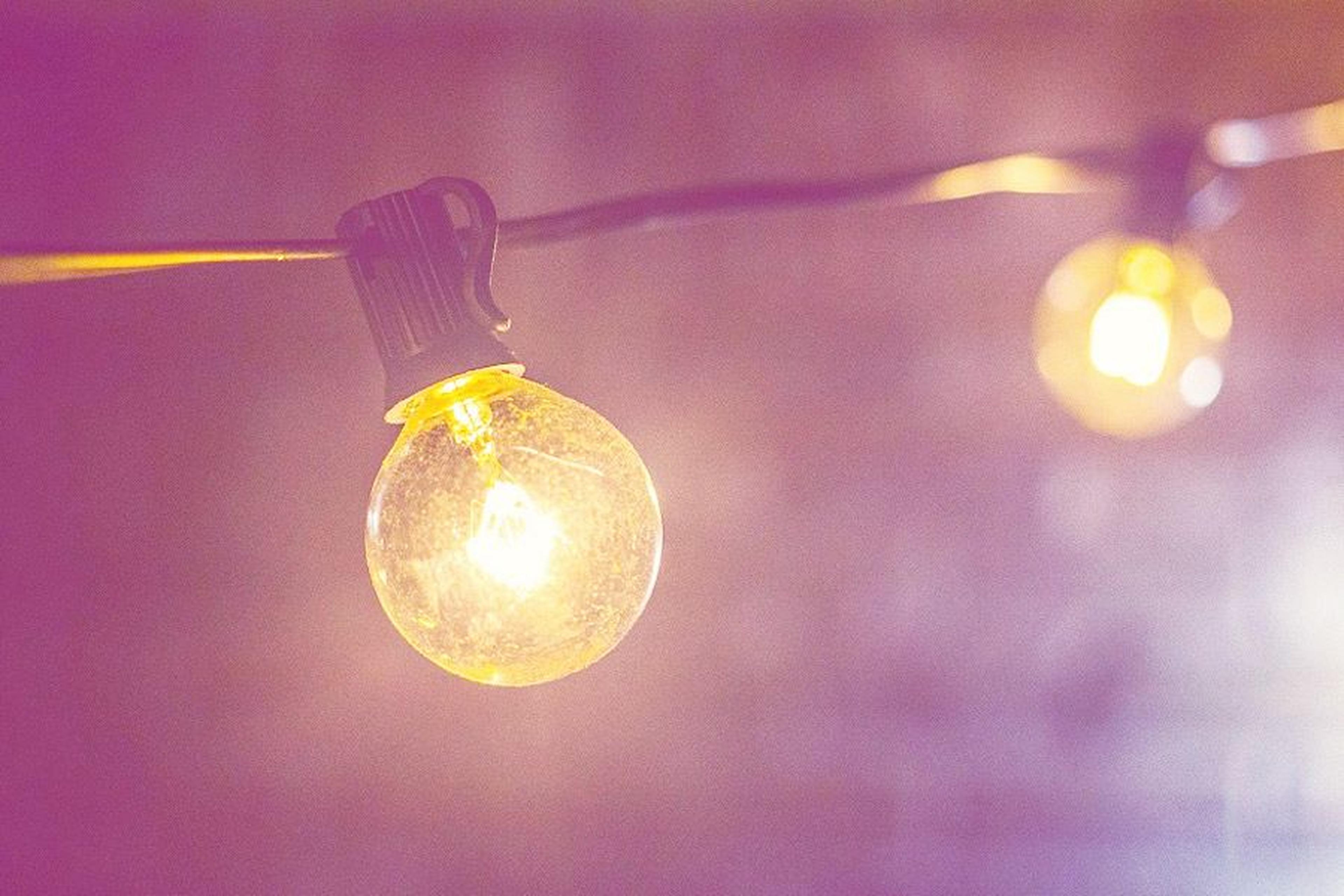 Nahaufnahme einer leuchtenden Glühbirne, die an einer Schnur vor einem unscharfen Hintergrund hängt und eine warme, sanfte Atmosphäre schafft.