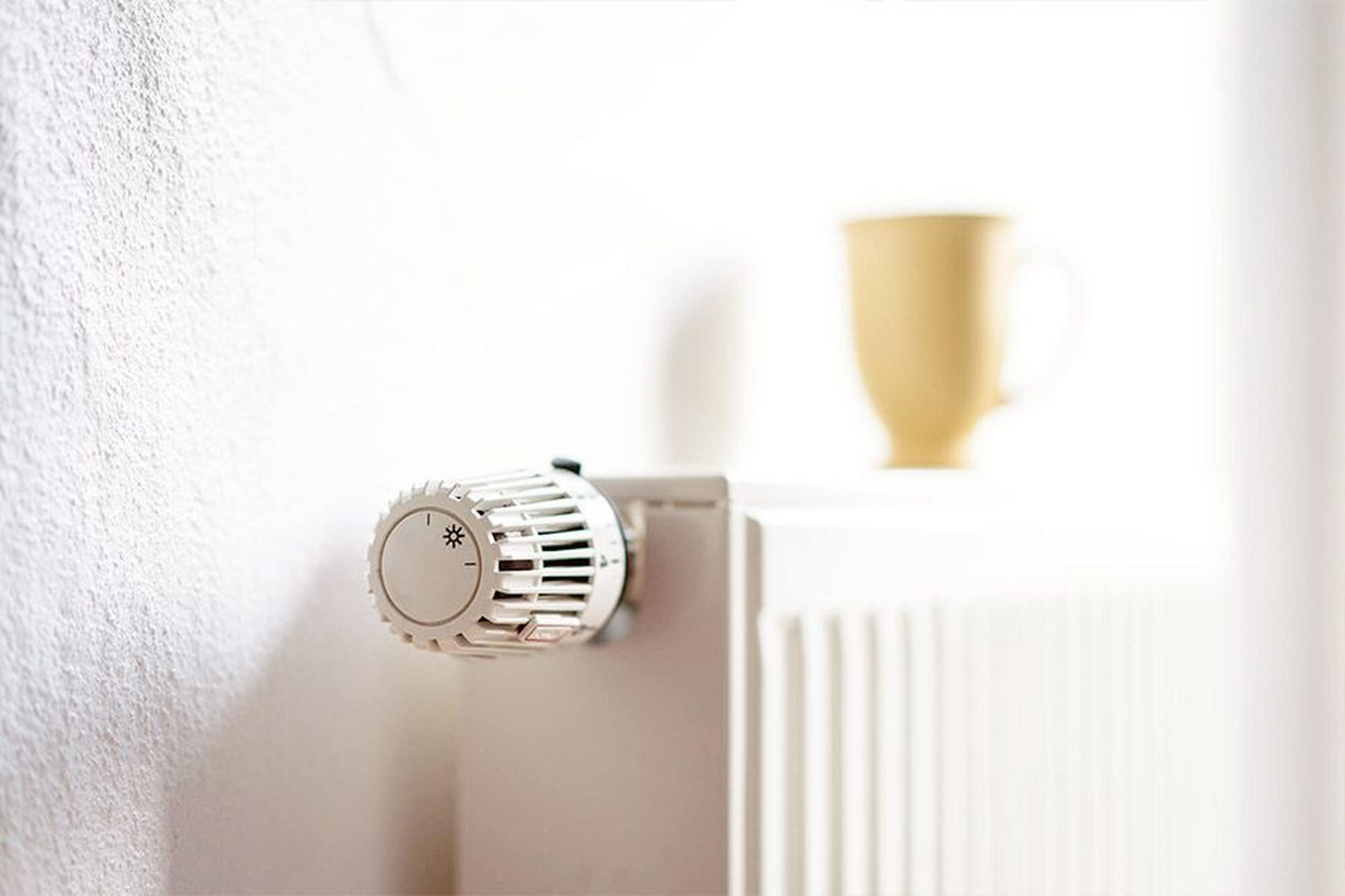 Heizkörper mit Thermostat an einer weißen Wand, darauf steht eine gelbe Tasse