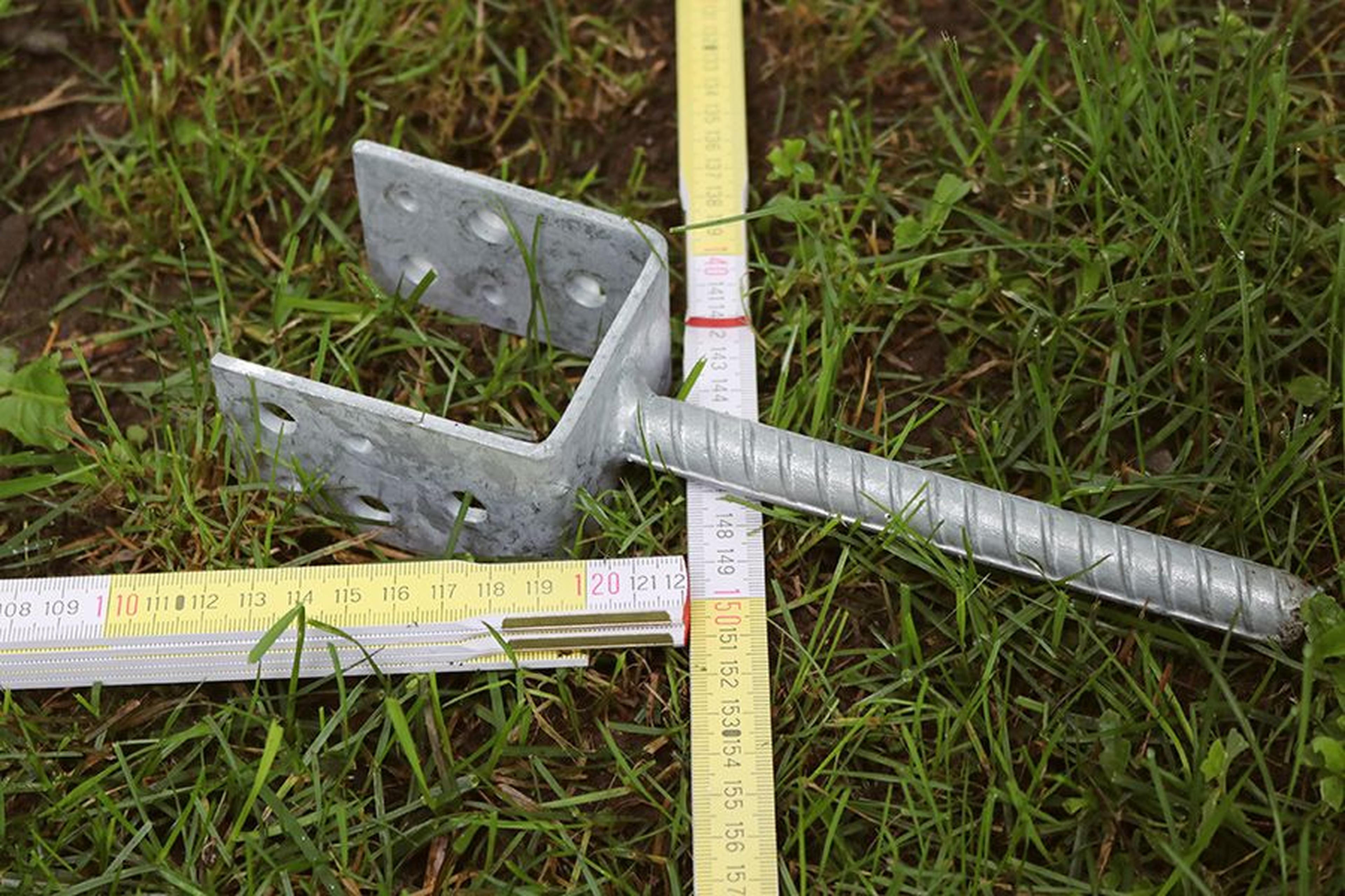 Metallhalterung auf Gras mit zwei Maßbändern, die die Abmessungen anzeigen.