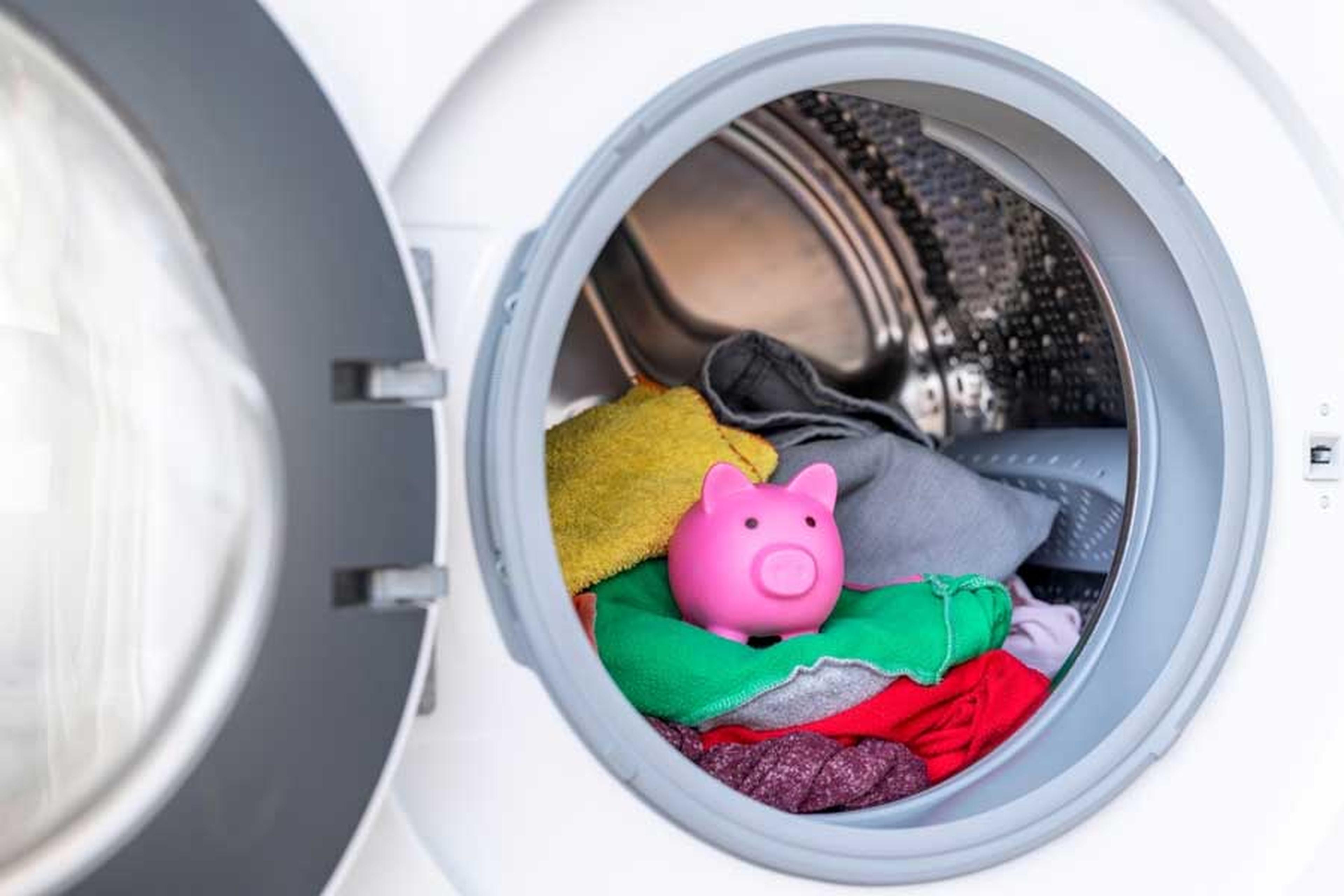 Waschmaschine mit geöffneter Klappe, in der Trommel bunte Wäsche und Sparschwein