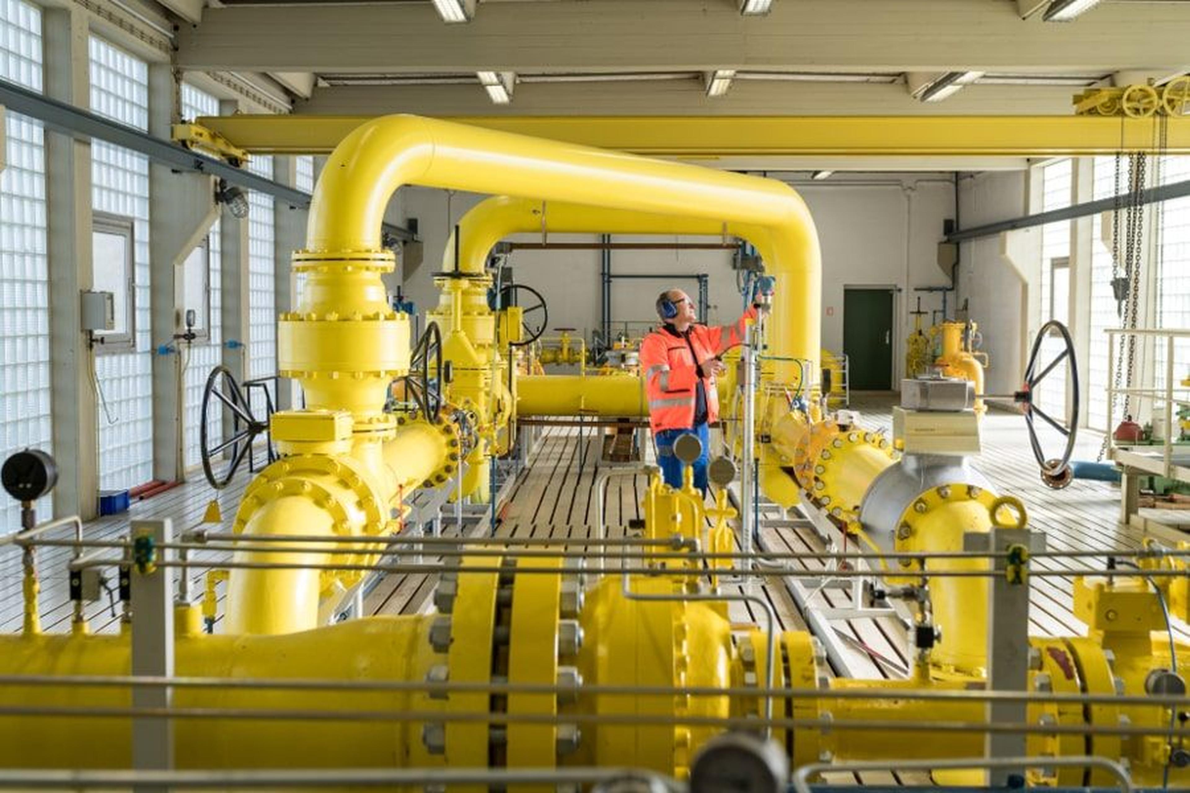 Ein Arbeiter in Sicherheitsausrüstung inspiziert große gelbe Industrierohre in einer geräumigen, gut beleuchteten Halle mit hohen Decken und Metallkonstruktionen.