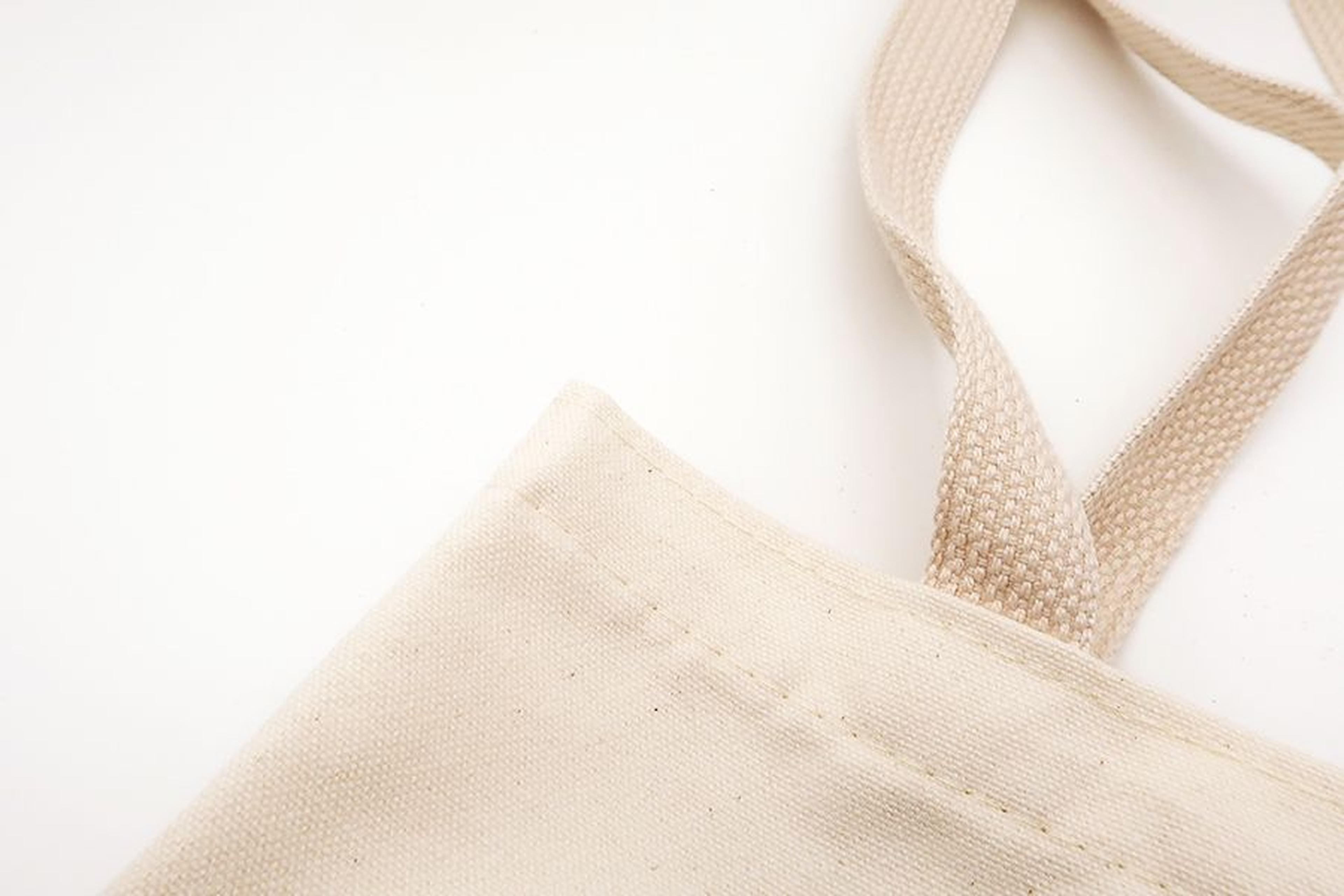 Nahaufnahme einer beigen Canvas-Tragetasche mit stabilen Griffen auf weißem Hintergrund.