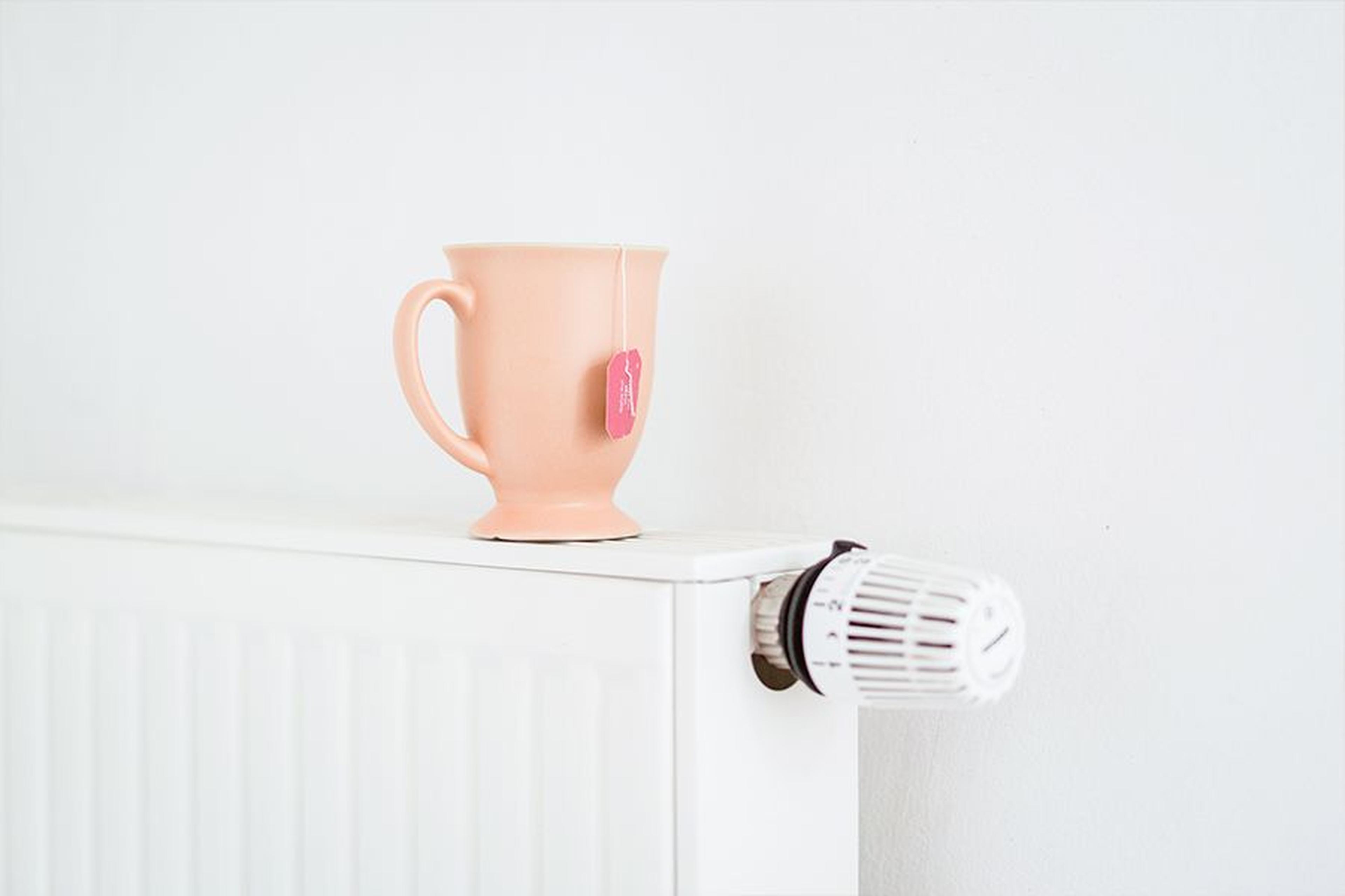 Heizkörper mit Thermostat, darauf steht eine Tasse mit Teebeutel