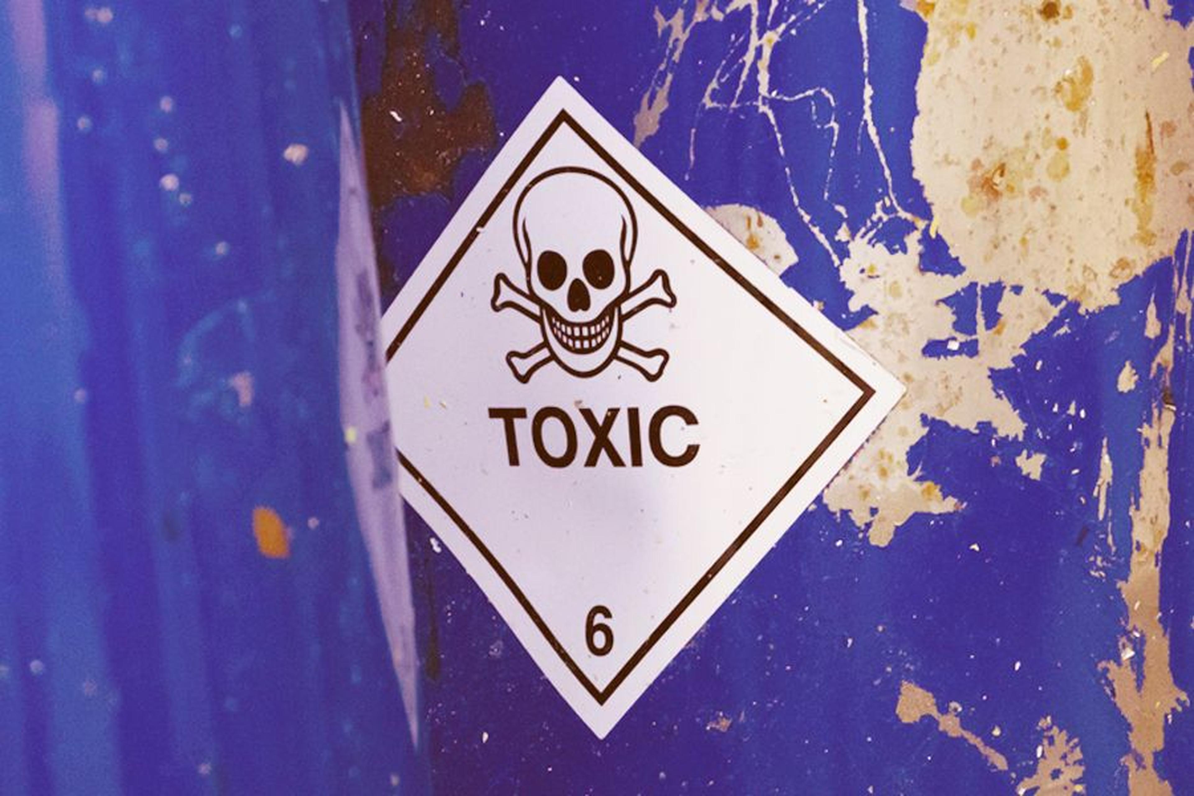 Warnschild mit Totenkopf und der Aufschrift „TOXIC“ an einem blauen Behälter.