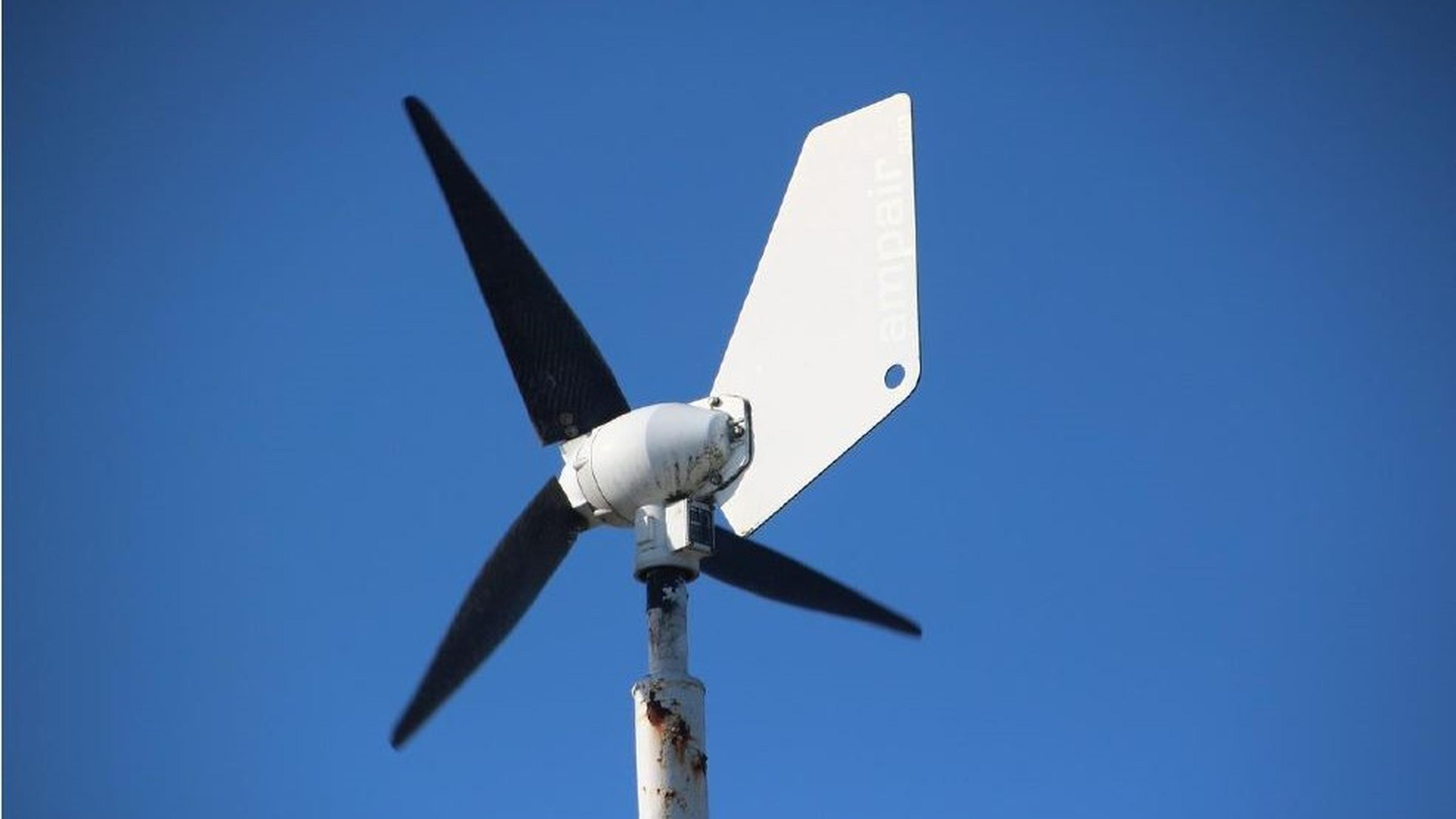 Eine kleine Windkraftanlage mit drei schwarzen Rotorblättern und einem weißen Heck vor einem strahlend blauen Himmel.