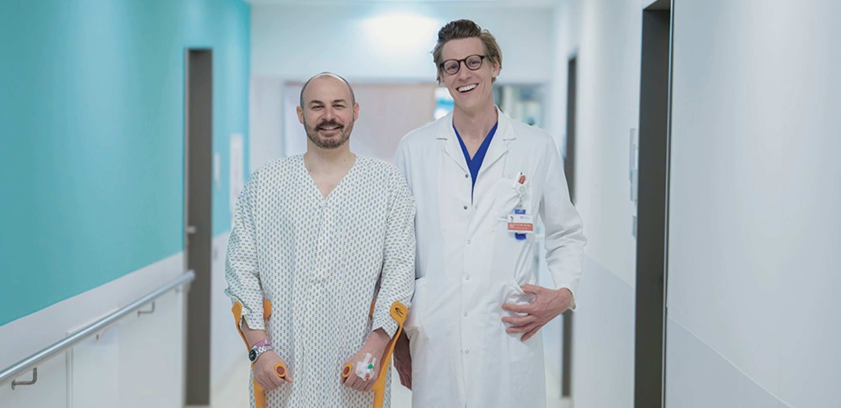 Patient nach Gelenks-OP mit Chirurgen, stehen im Krankenhausgang