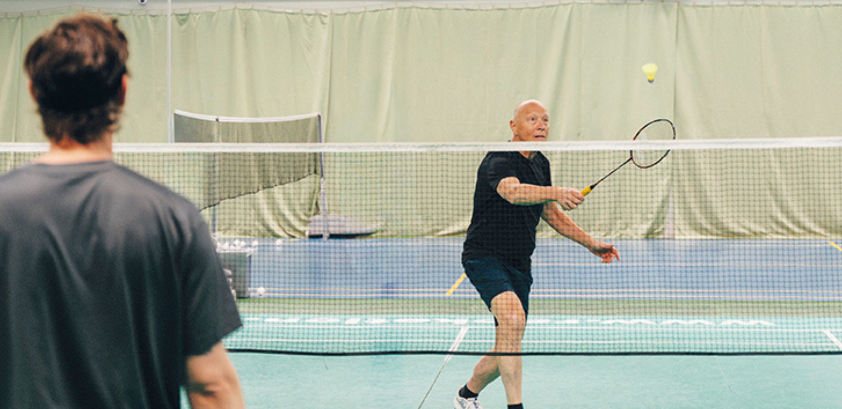 Zwei Männer spielen Badminton in einer Halle.