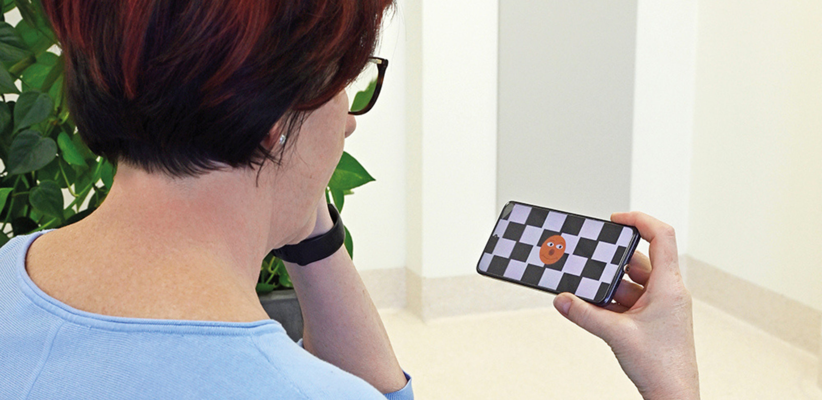 Frau sieht auf Handy mit orangen Punkt und schwarz-weißem Schachbrett-Muster
