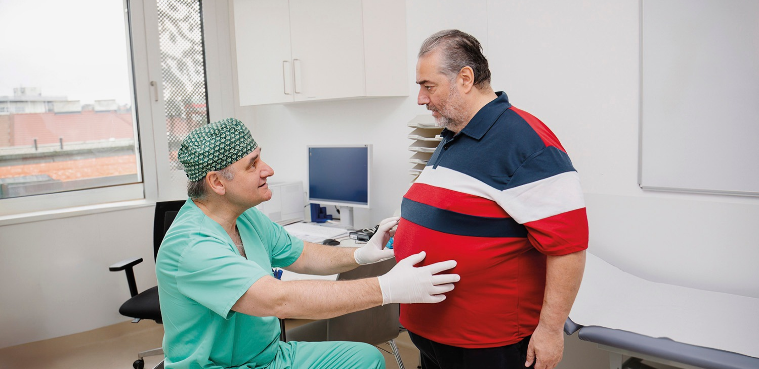 Arzt sitzt und sieht sich Bauchbereich von stehendem Patienten an