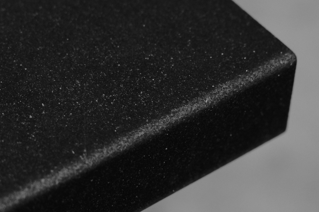 Nahaufnahme einer schwarzen, strukturierten Oberfläche mit einem leicht erhöhten Rand auf der rechten Seite.