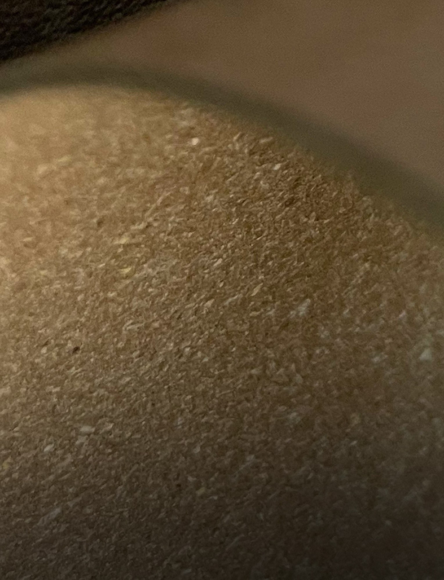 Close-up view of a textured, beige surface with a subtle pattern and a small, dark spot.