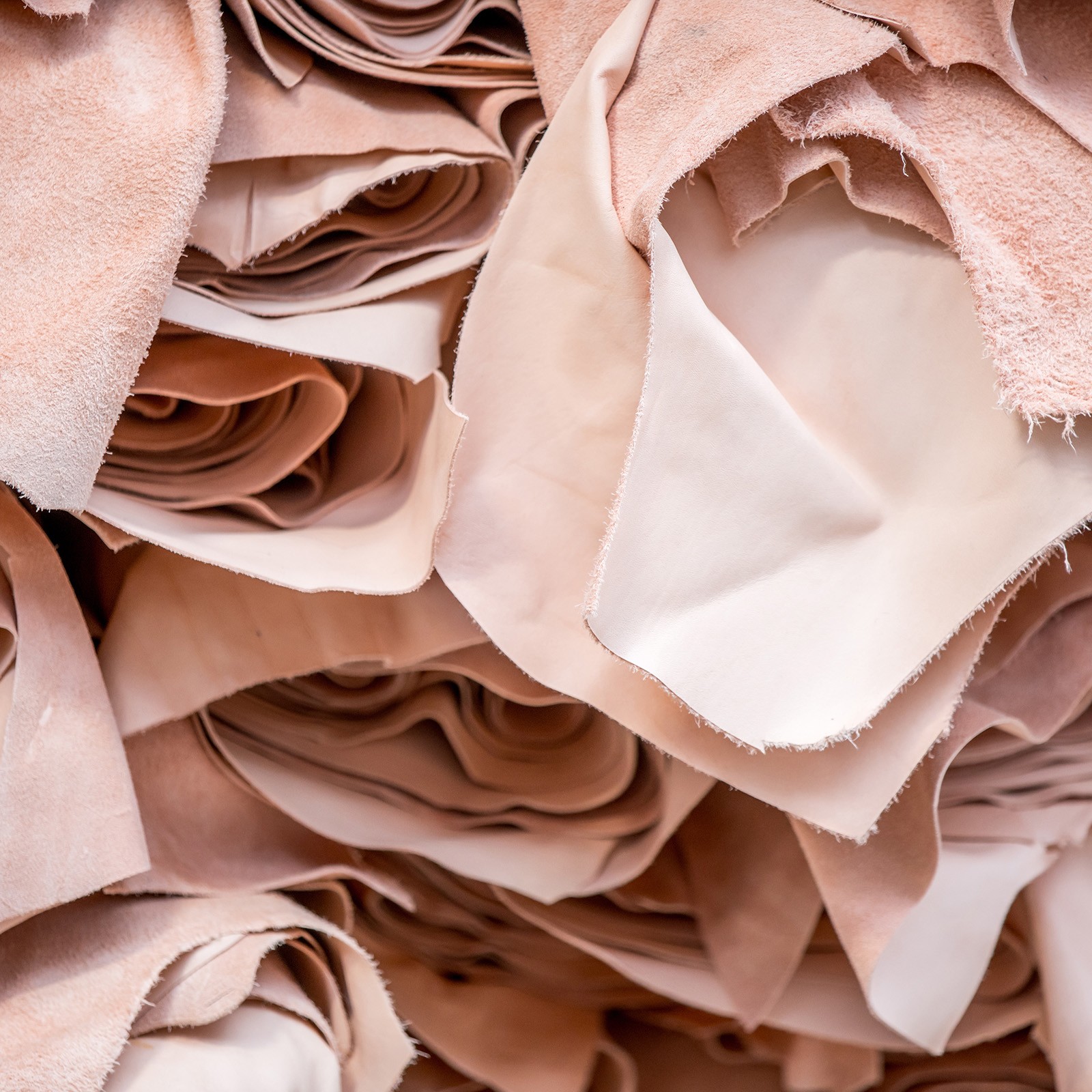 A close-up of a pile of soft, pink, and brown leather sheets, showcasing their texture and color variations.