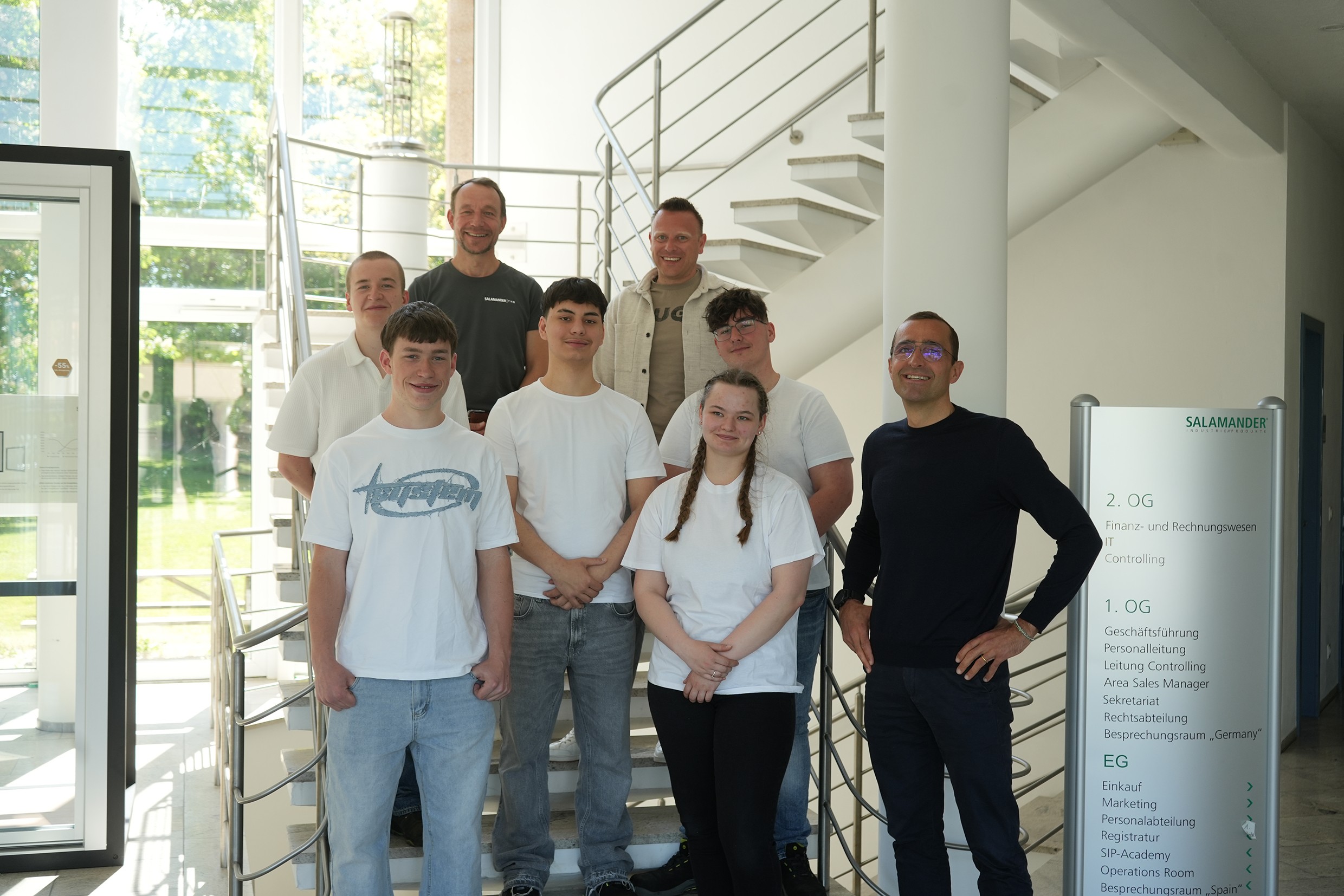 Um grupo de pessoas está de pé nas escadas em frente a um edifício. Eles estão sorrindo e posando para uma foto.