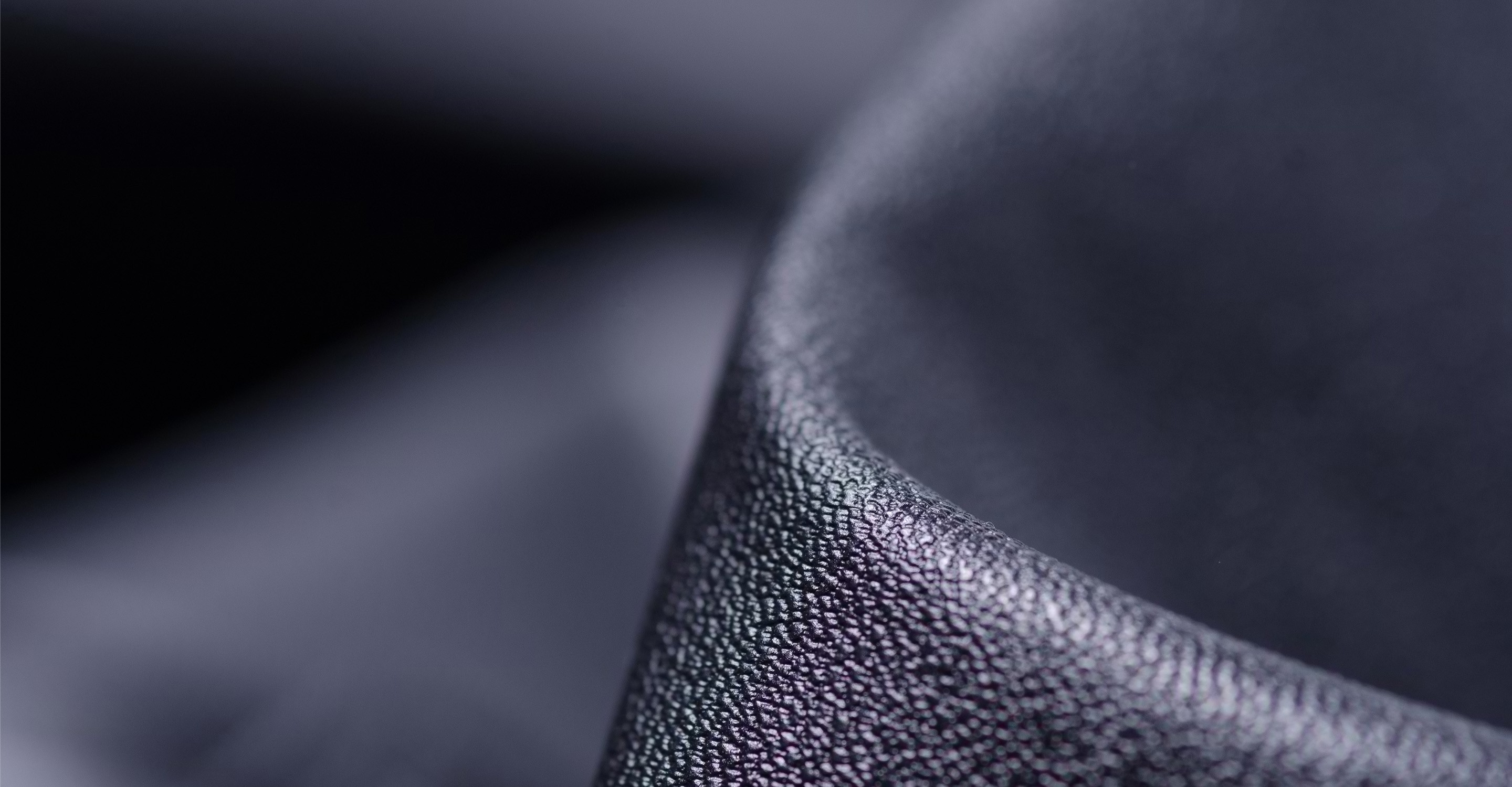 A close-up view of a black leather seat with a textured surface and a slightly curved edge.