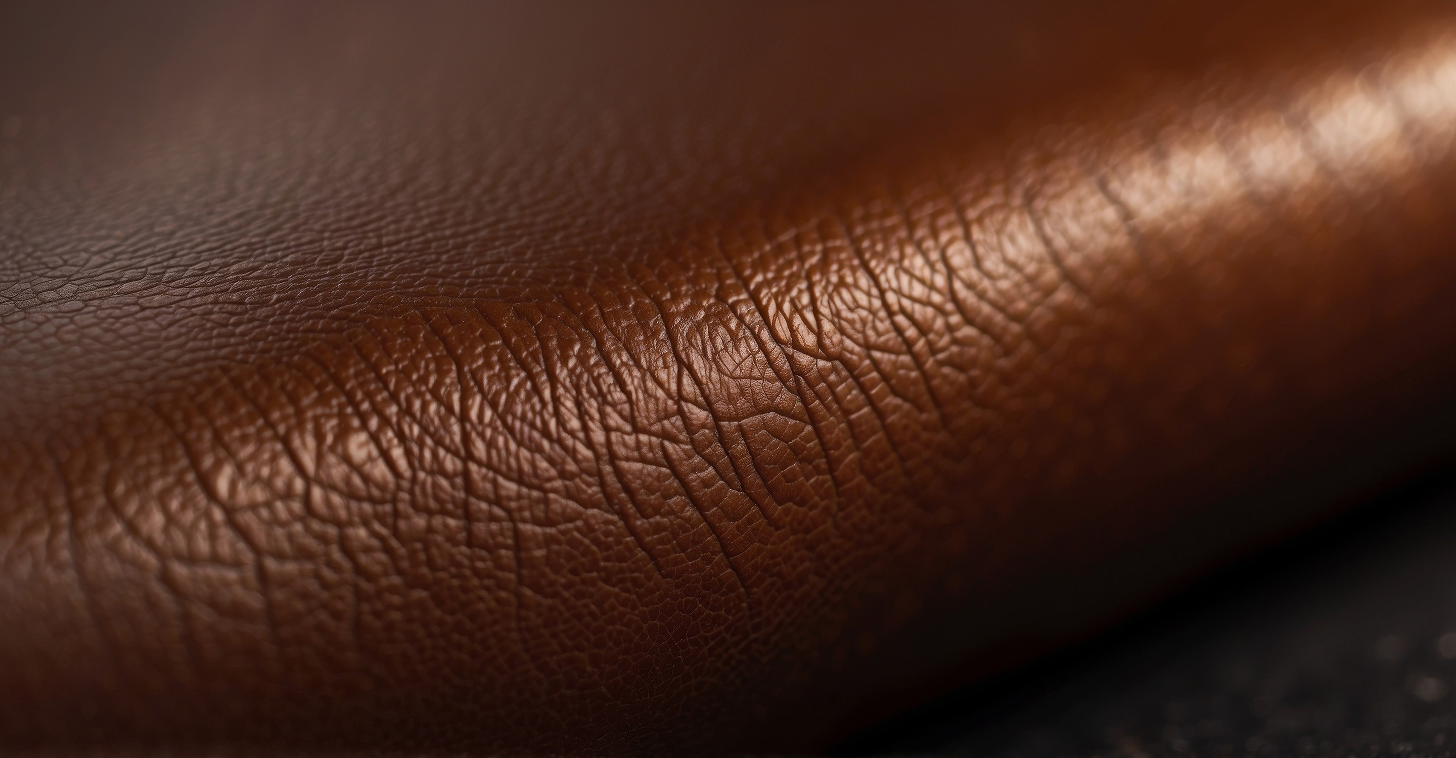Close-up view of a brown leather surface with visible grain and texture, highlighting its natural and luxurious appearance.