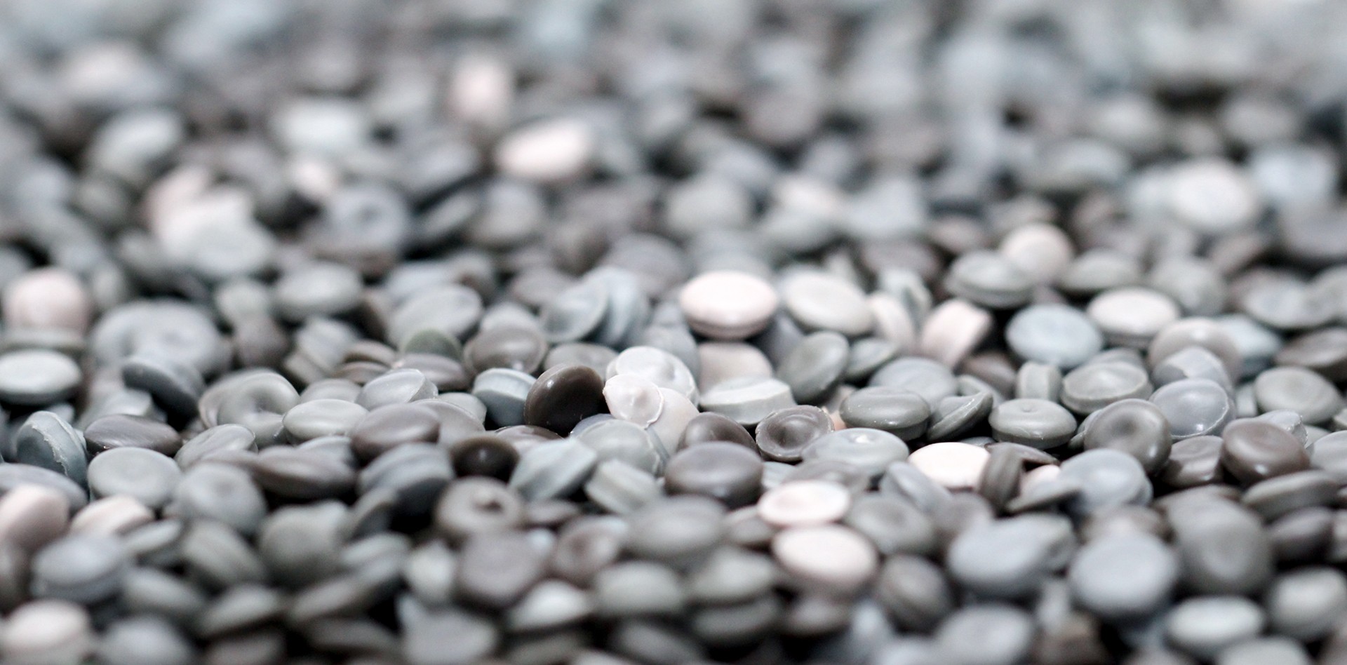 Una vista cercana de un montón de gránulos de plástico gris y blanco, posiblemente reciclados o materia prima para la fabricación.