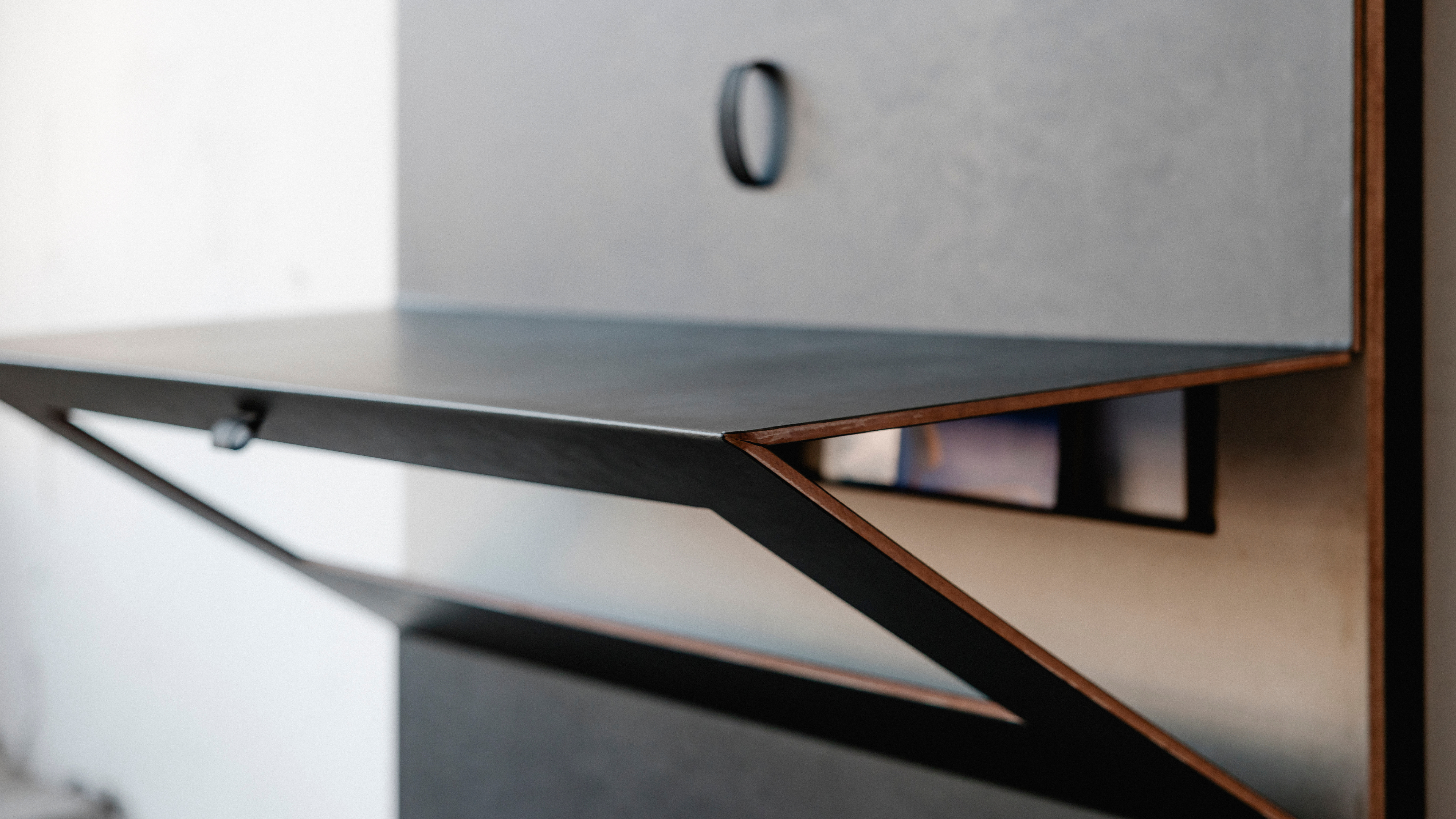 Eine Nahaufnahme eines schwarzen und braunen Regals mit einer Nummer 0 darauf. Das Regal ist an einer Wand befestigt und hat eine kleine quadratische Öffnung auf der rechten Seite. Das Regal besteht aus Metall und hat einen Holzrahmen. Die Wand hinter dem Regal ist weiß.