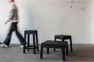 Eine Person, die an drei schwarzen Hockern in einem Raum mit einer weißen Wand vorbeigeht.