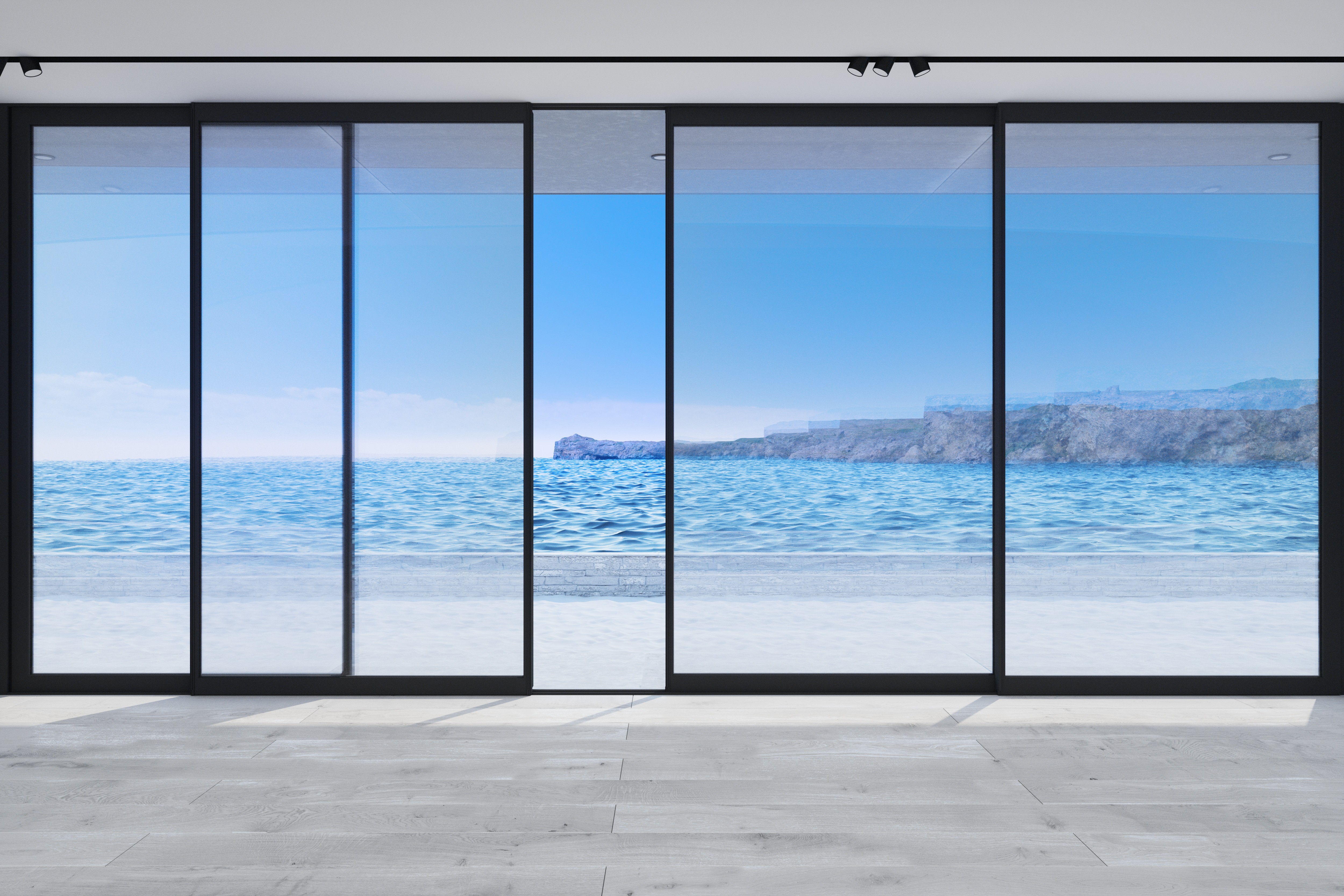 A room with large black sliding glass doors that open to a balcony overlooking the ocean.