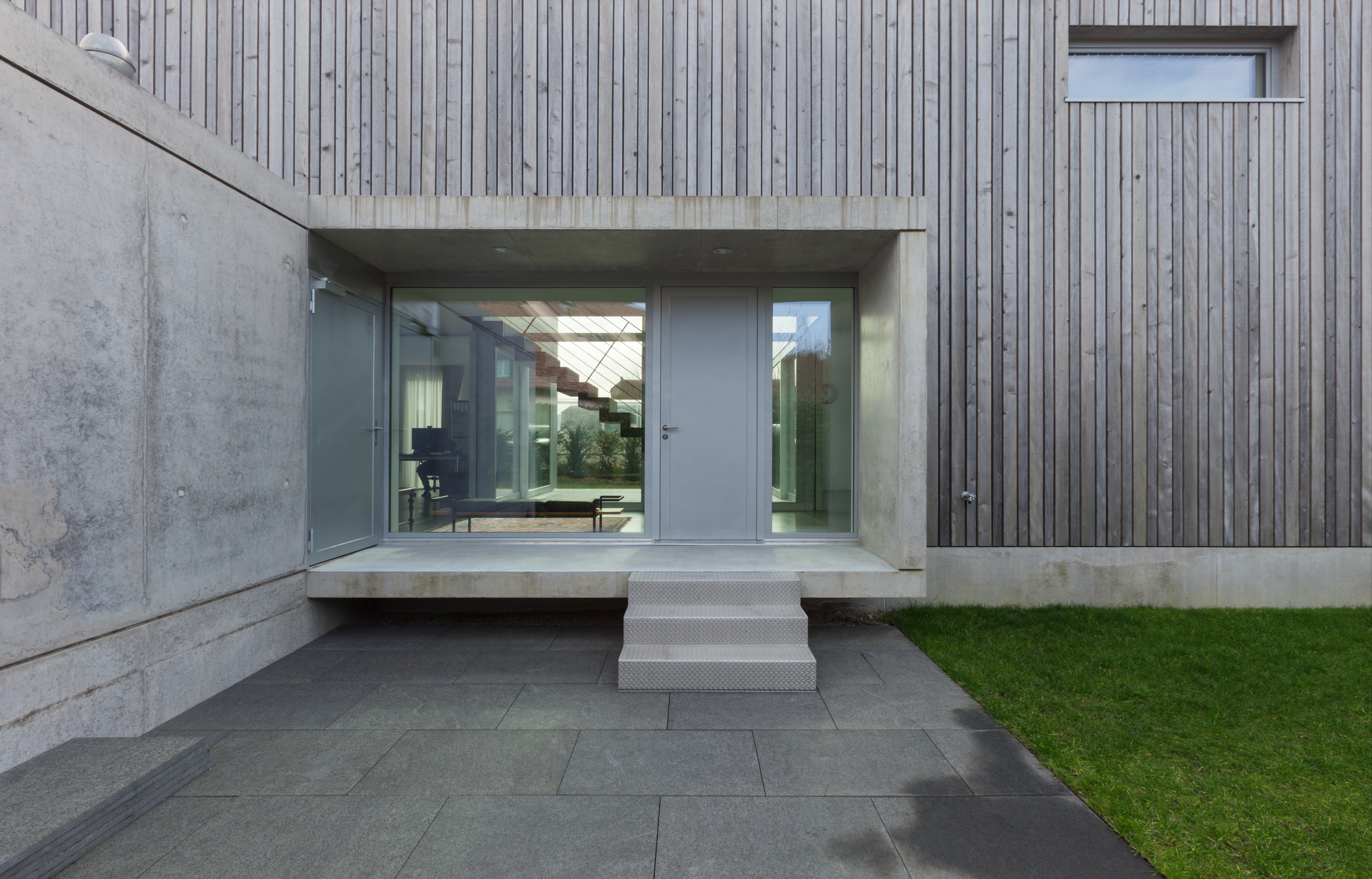 Exterior de una casa moderna con una pared de madera, puertas de vidrio y un camino de concreto que conduce a la entrada.