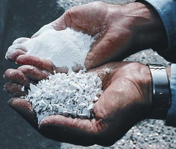 Hands holding white crushed stone, with one hand holding a larger piece and the other holding smaller pieces.