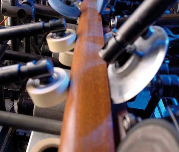A close-up view of a wooden board being processed on a machine with rollers and tape.