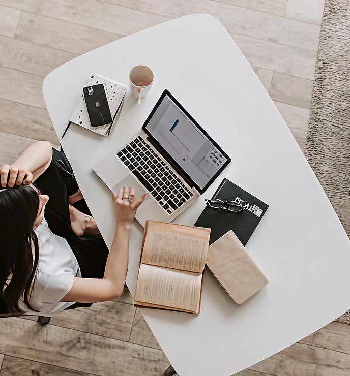 Eine Frau sitzt an einem Tisch mit einem Laptop, einer Tasse Kaffee und Büchern.