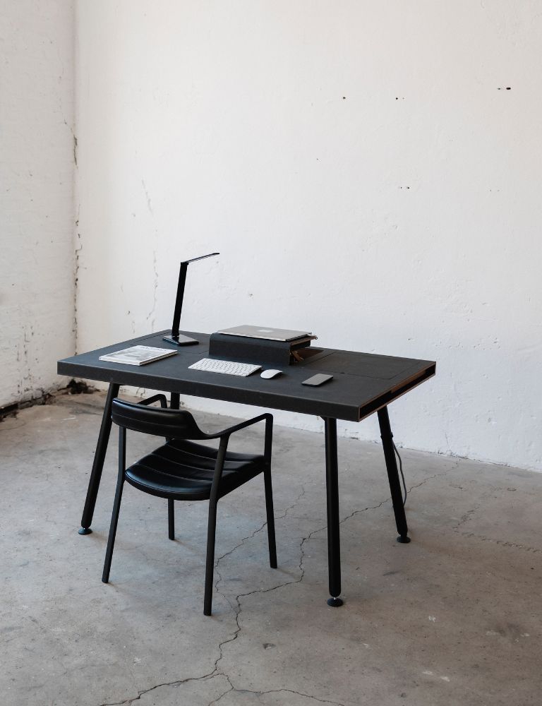 Black desk with a computer keyboard, mouse, lamp, and books on top, next to a black chair.