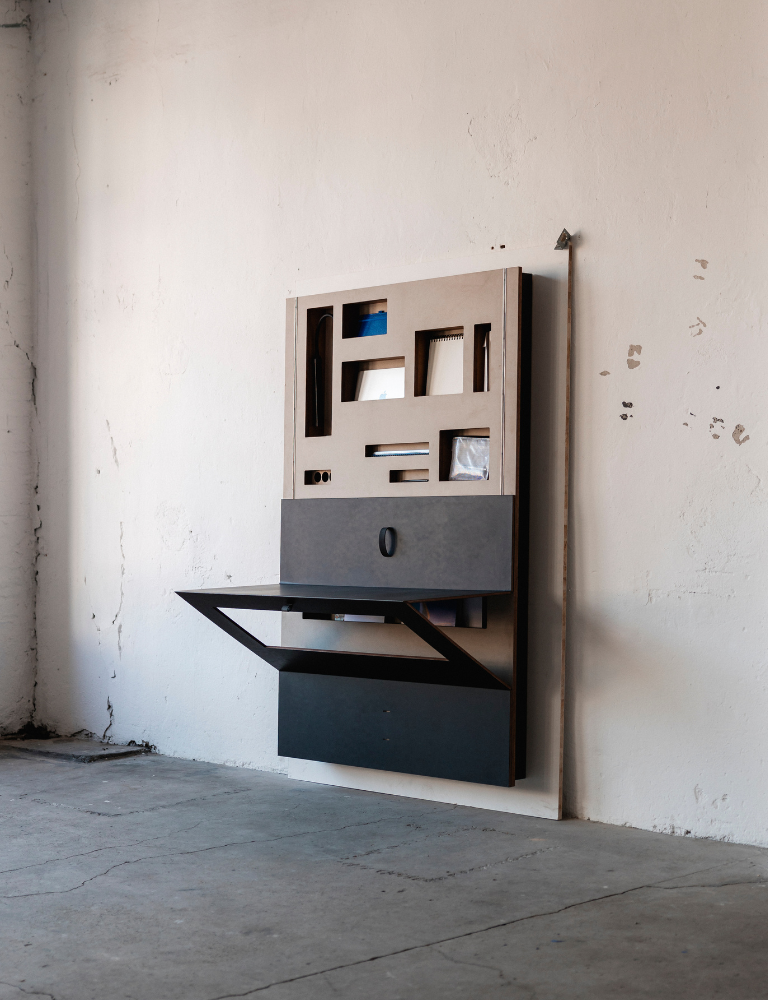 A wall-mounted desk with a black base and a white top, featuring a built-in shelf and a small cabinet with a door.