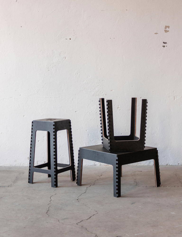 Two black stools with geometric designs, one with a seat and the other with a backrest, placed on a concrete floor against a white wall.