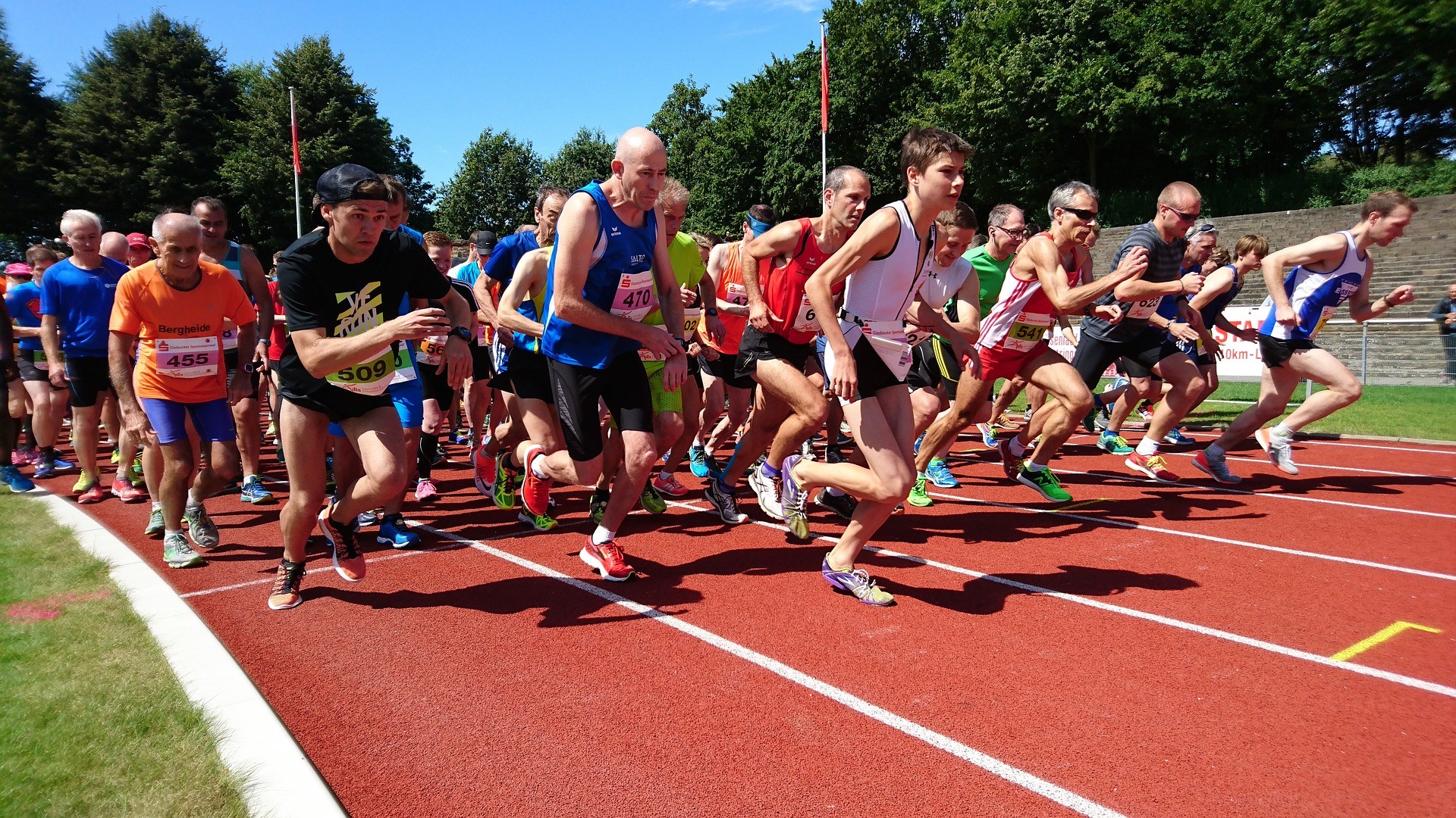 A group of runners are running on a track during a race. They are wearing numbered bibs and running shoes.