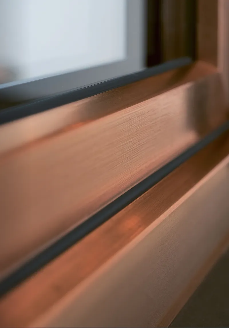 Vista de cerca de un marco de ventana de cobre con un borde negro y un panel de vidrio blanco.