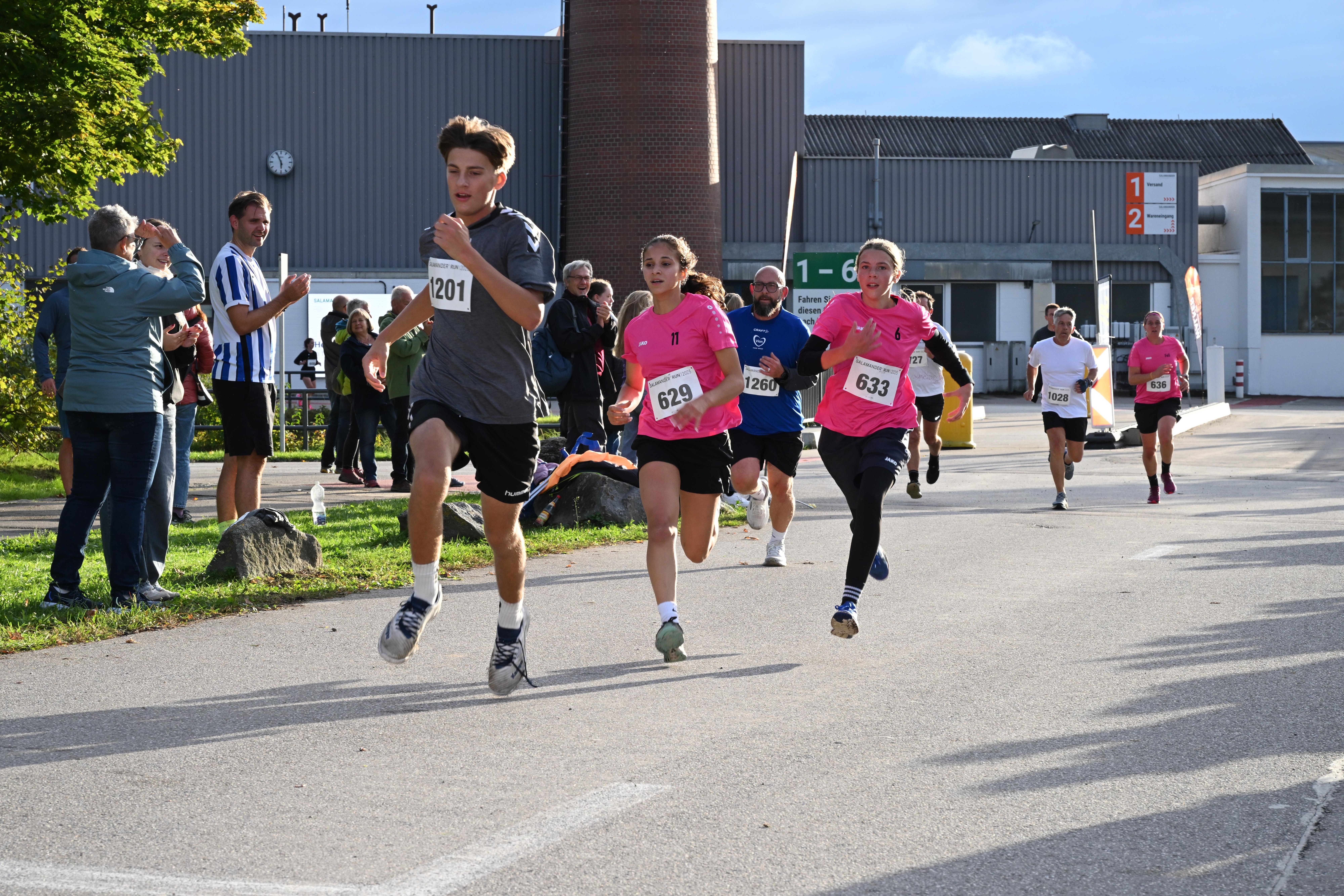 A group of runners in a race with spectators on the side of the road.