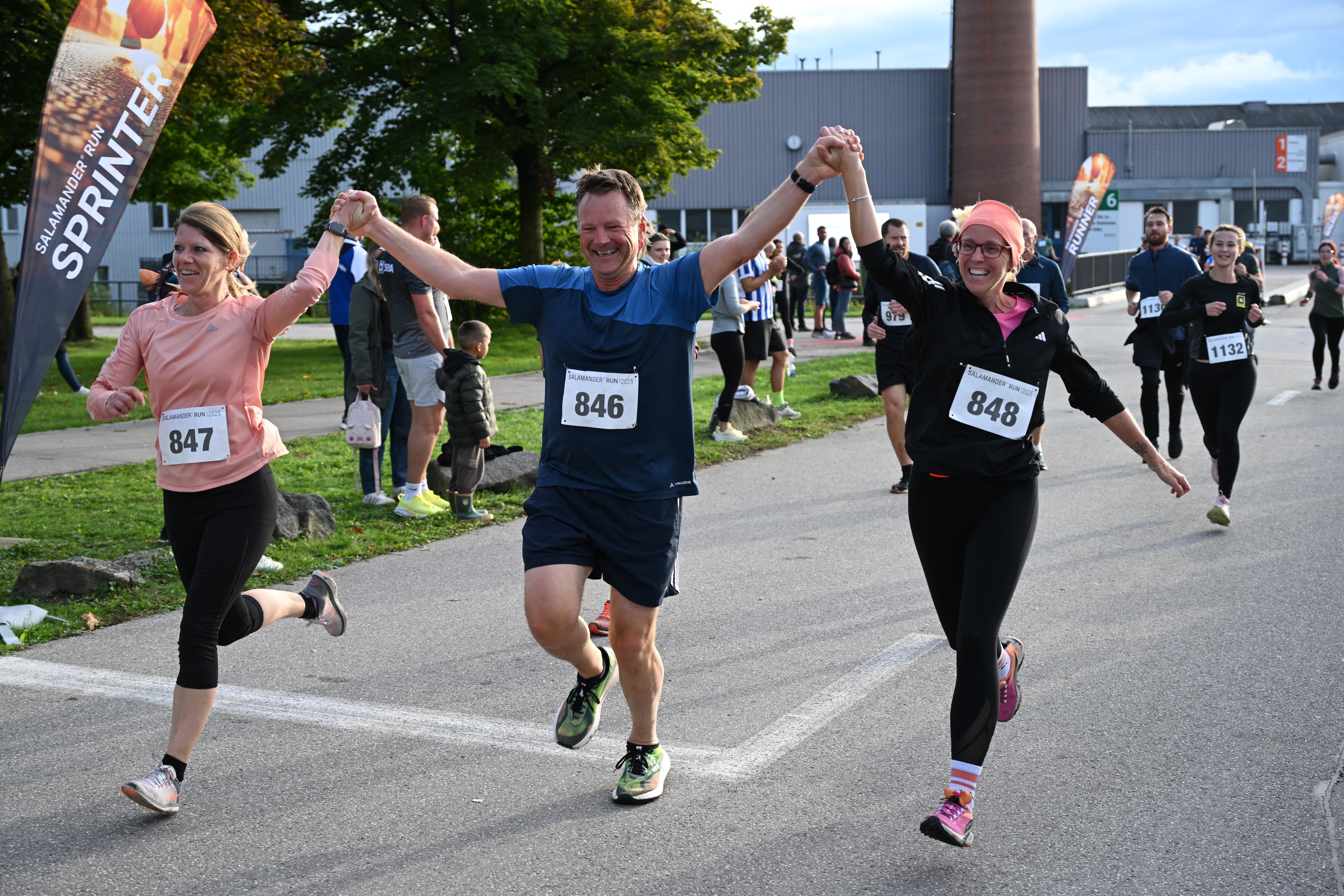 Three runners with numbers 846, 847, and 848 hold hands as they run in a marathon.