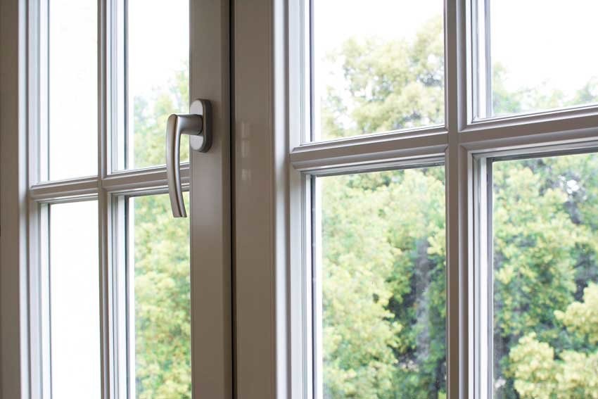 A close-up view of a white window with a metal handle and a view of trees outside.