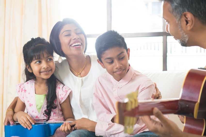 A family of four, consisting of a mother, father, and two children, is sitting on a couch and playing guitars together.
