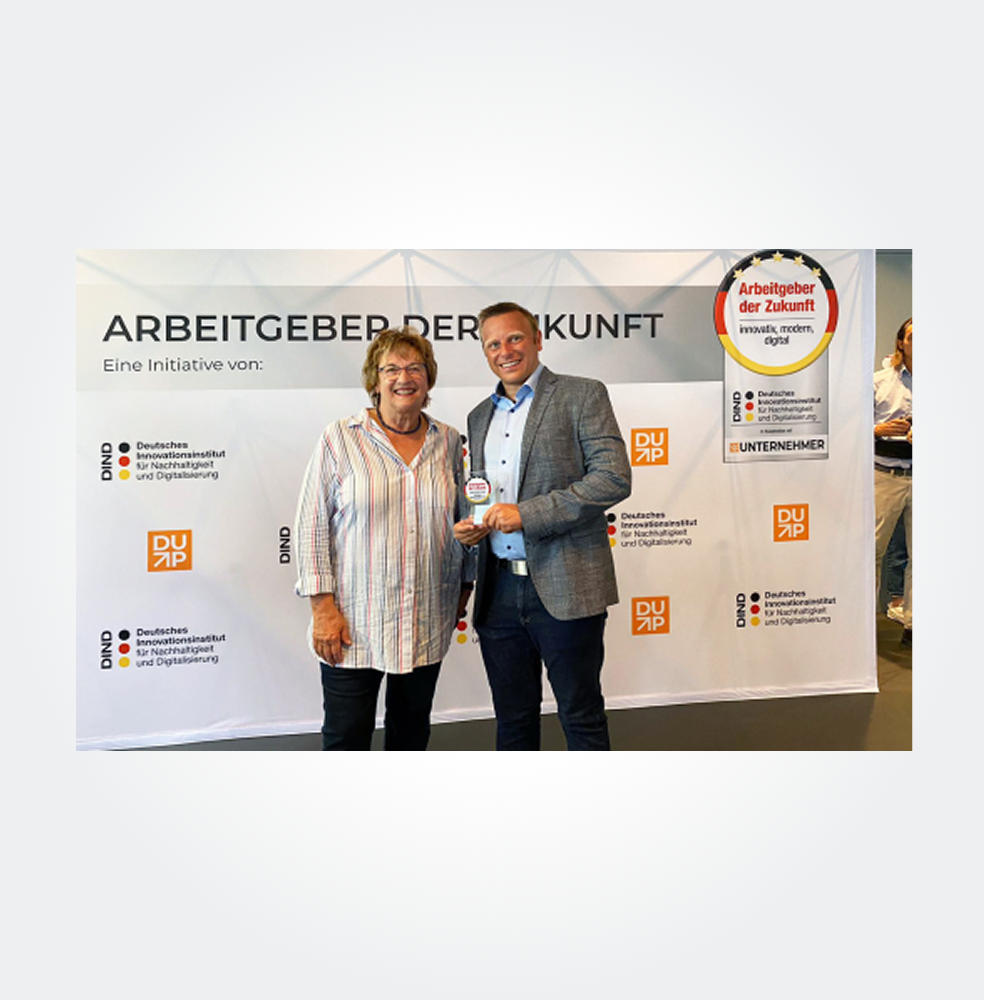 Zwei Personen stehen vor einem Banner mit dem Text "Arbeitgeber der Zukunft" und einem Logo.