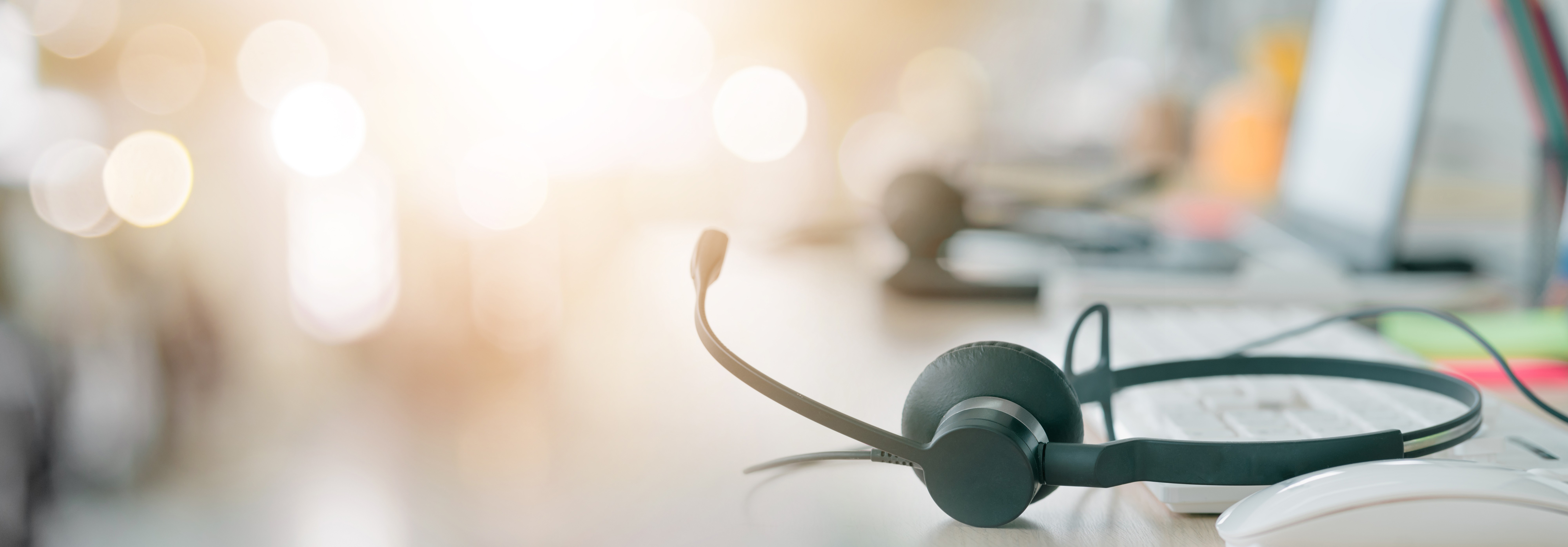 A black headset microphone is placed on a desk with a computer keyboard and mouse in the background.