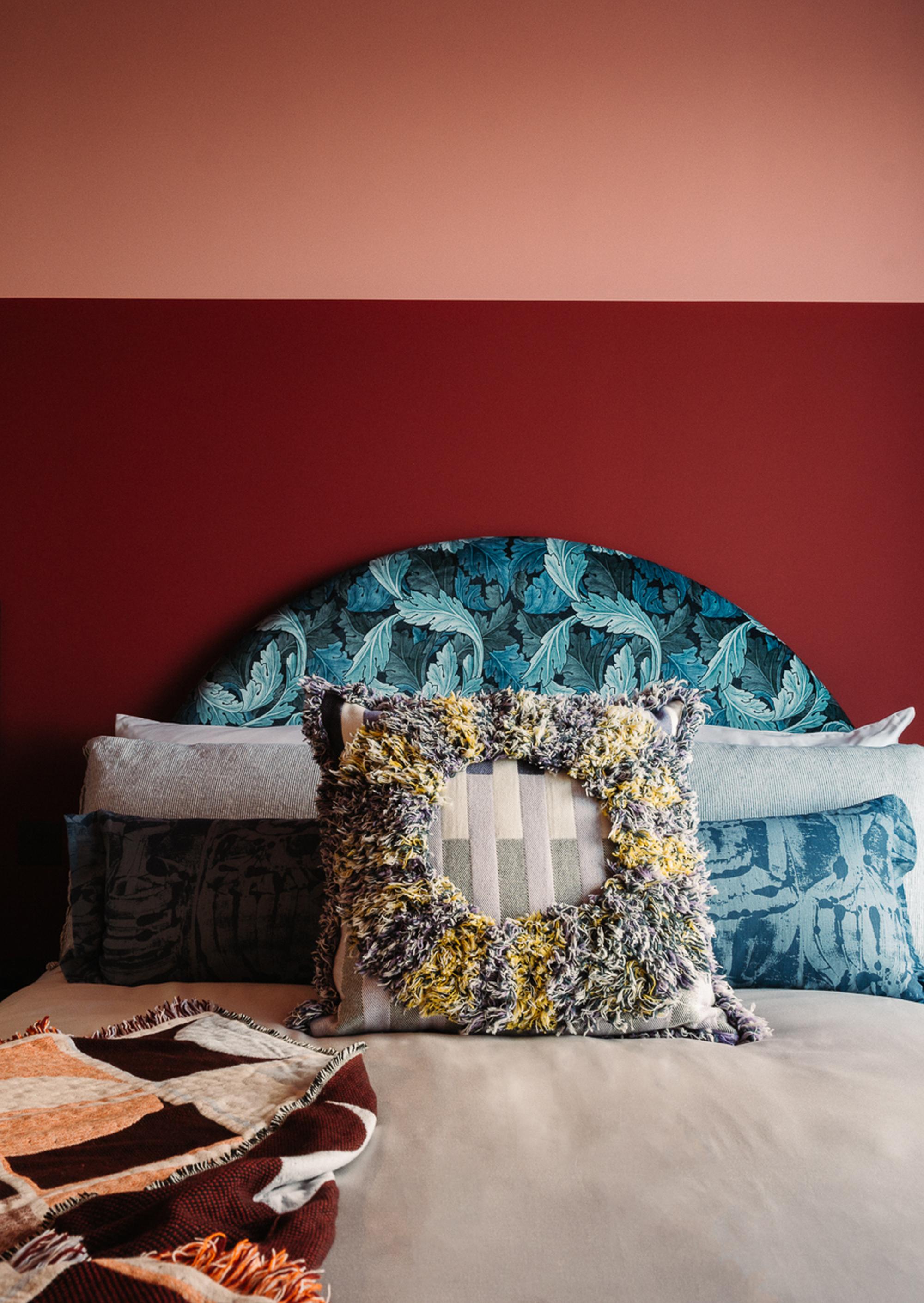 A photo of a bed in a bedroom at The Eades with a turquoise patterned headboard, sheer blue curtains and pink and red painted wall.