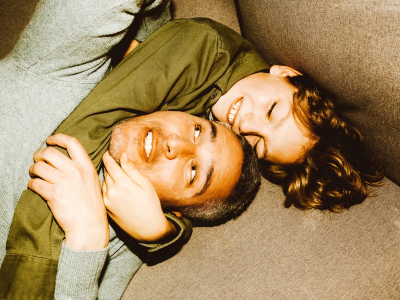 Vater und Sohn sitzen auf dem Sofa und lachen; der Sohn umarmt den Hals des Vaters.