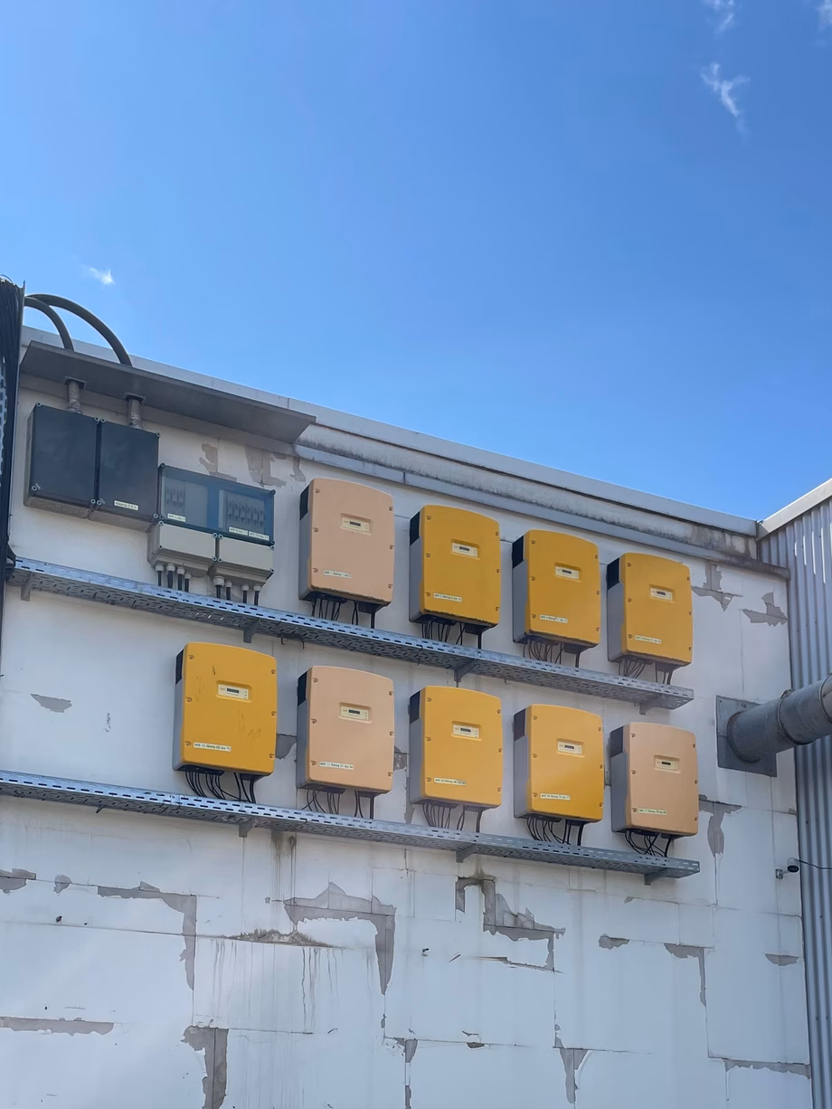 Yellow electrical boxes mounted on an industrial building exterior, with cables and a metal pipe under a blue sky.