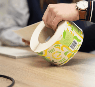Person peeling a bright green and yellow product label from a large roll on a wooden desk.