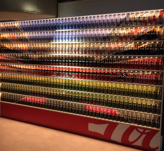 Backlit store display with multiple shelves of colorful glass soda bottles arranged in neat horizontal rows.