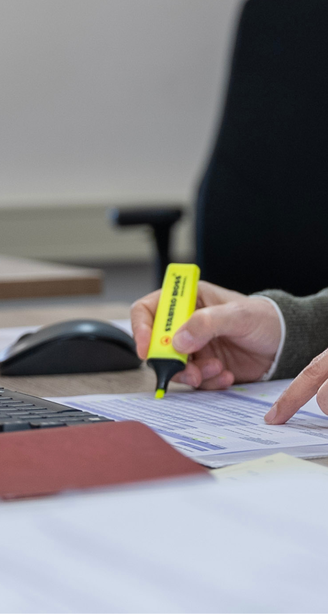 Person at a desk highlighting text on a printed document beside a keyboard, mouse, coffee cup, and smartphone.