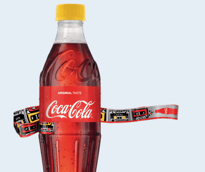 Een plastic fles Coca-Cola met een gele dop, omwikkeld met een kleurrijk etiket met een patroon van cassettebandjes op een lichtgrijze achtergrond.