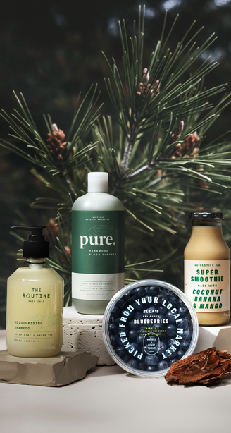 A collection of skincare and food products, including lotions and smoothies, displayed on natural materials with a pine tree background.