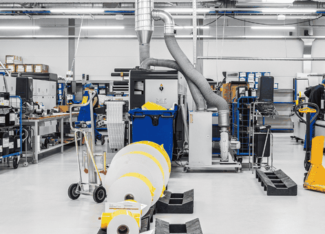 Een lichte, overzichtelijke fabrieksvloer met industriële machines, karren en grote papierrollen in een schone, moderne productieomgeving.