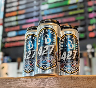 Four Baxbier Brewery 427 IPA cans on a wooden counter with a colorful, blurred tap list in the background.